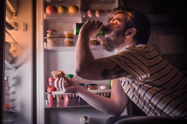 Person eating in front of open refrigerator door