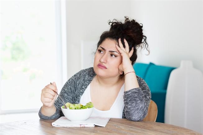 Young woman unhappy eating salad