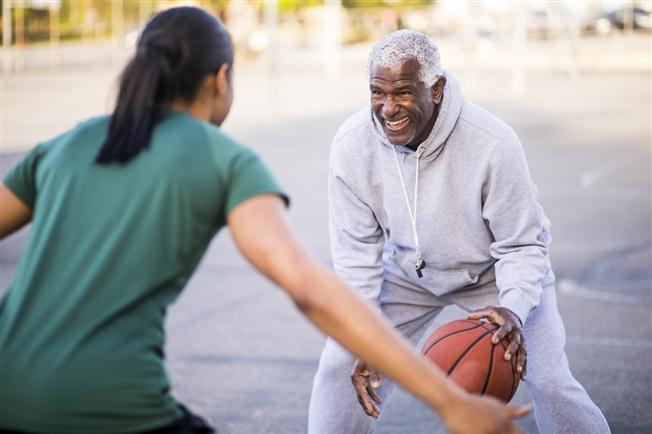 Young adult woman and older gentleman playing basketball outside