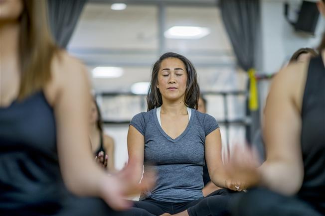 Woman sitting in a mindful meditation pose with foreground people around her out of focus