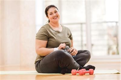 Woman sitting on yoga mat holding her water bottle with small weights sitting in front of her
