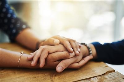 People comforting one another (picture shows close up on their clasped hands on a table)