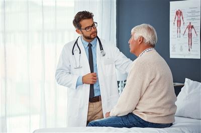 Older man sitting in doctor's office with doctor standing nearby with hand on patient's shoulder