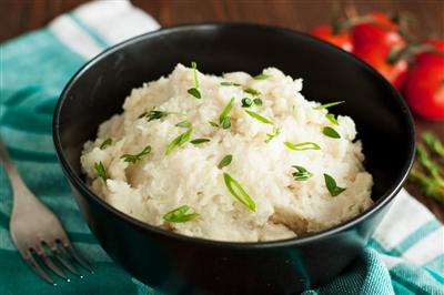 Mashed cauliflower with garlic, thyme and scallion in black bowl on wooden table