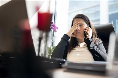 Woman sitting at desk showing physical symptoms of stress headache