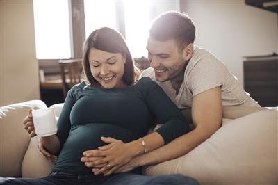 Man cradling pregnant wife's belly on couch