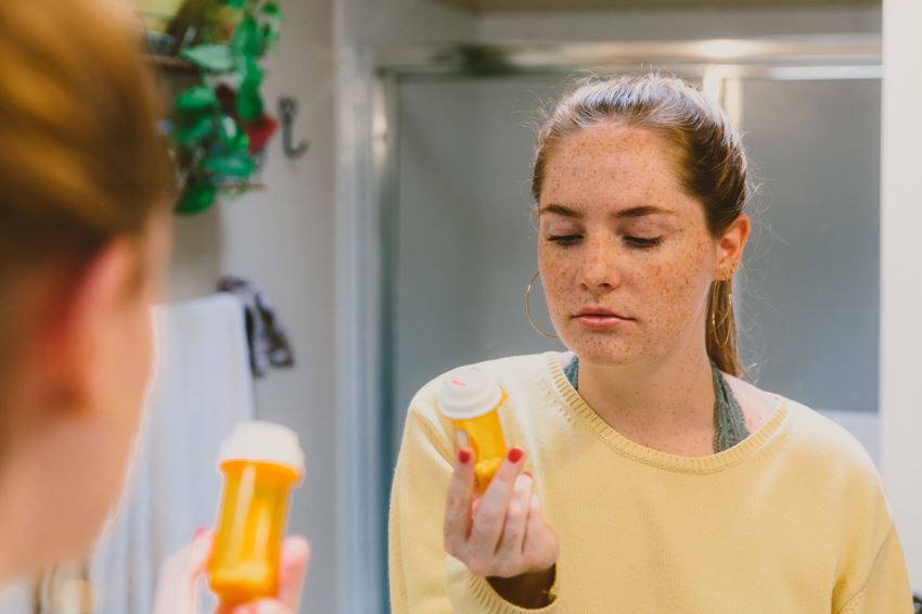 Young woman reading back of pill bottle from medicine cabinet