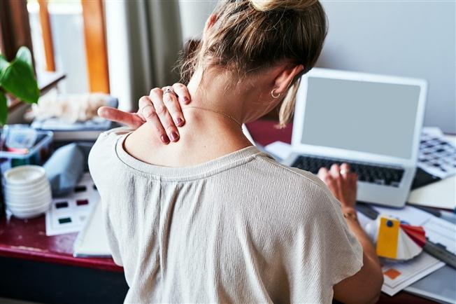 Rearview shot of a woman experiencing discomfort in her shoulders while sitting at her desk