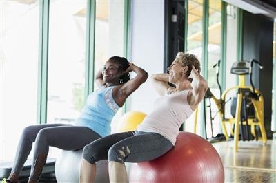 Two women at the gym on medicine balls talking during workout