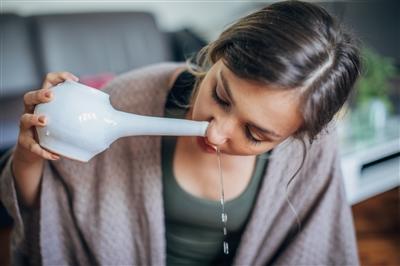 Young woman holding neti pot to nose for nasal irrigation