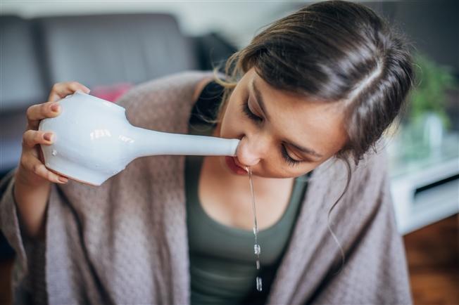 Young woman holding neti pot to nose for nasal irrigation