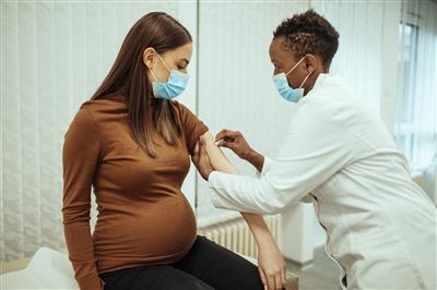 Young doctor giving COVID vaccine to pregnant woman in doctor's office