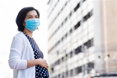 Pregnant woman outside wearing mask during COVID touching belly