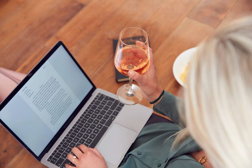 Woman drinking glass of wine while working on her computer