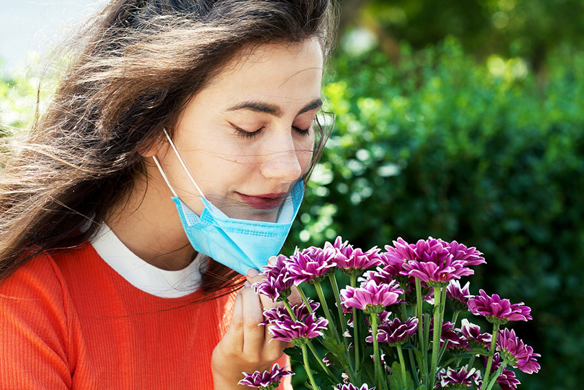 Young woman removing mask so she can smell the flowers