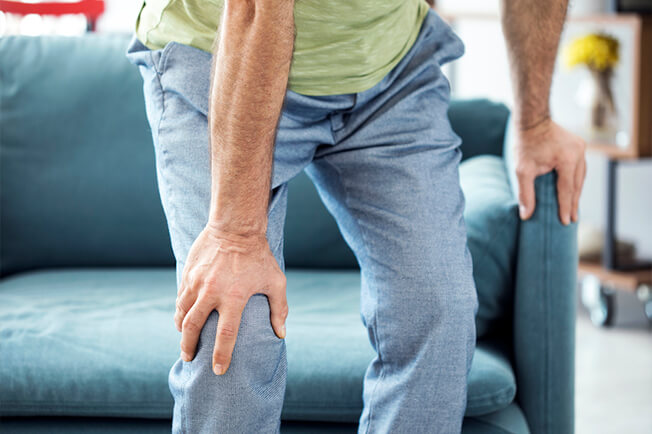 man getting up from sofa, holding knee