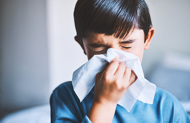 Young boy sneezing into a tissue