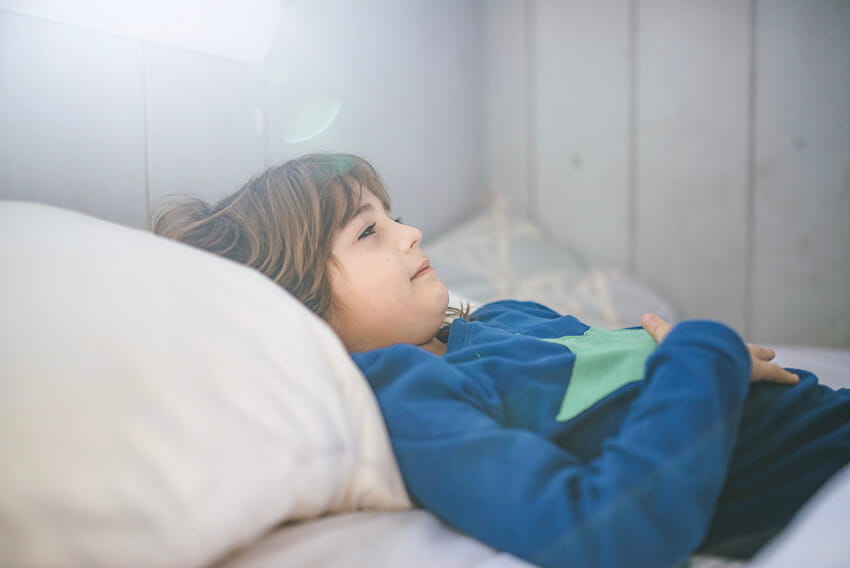 Kid in pajamas lays in bed feeling sick with stomach bug