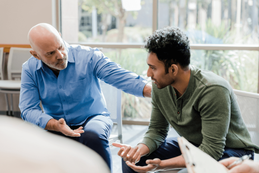 Older man with his hand on the arm of a younger man in therapy.