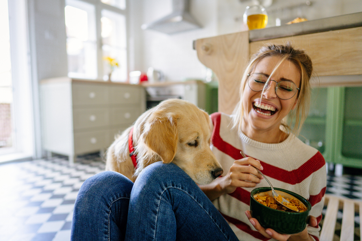 Young woman in her kitchen laughing with her dog.