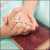 Hands folded over a bible holding a rosary