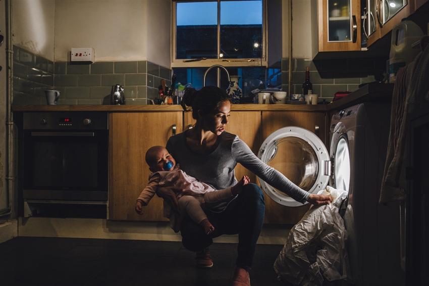 Multitasking mother holding baby and loading up washing machine