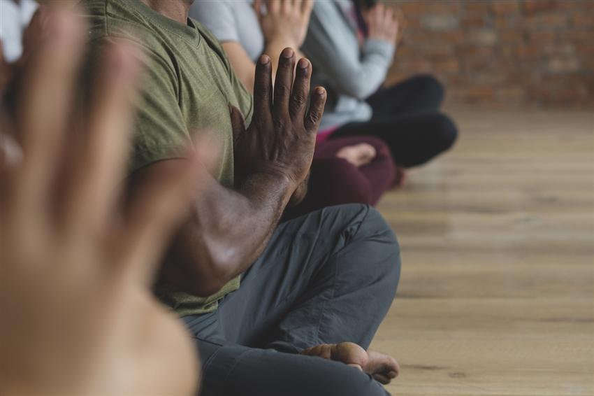 Close-up on meditating people sitting crossed-legged on the ground with hands together in front of them