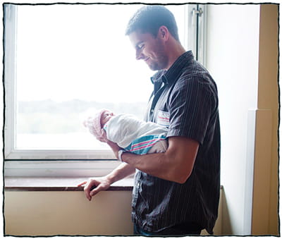 Father standing by window holding his newborn