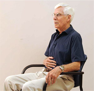 Man illustrating proper deep breathing technique while sitting in a chair
