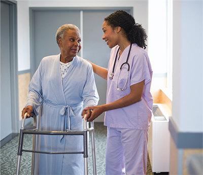 A nurse assisting a patient as she walks down a hallway with a walker